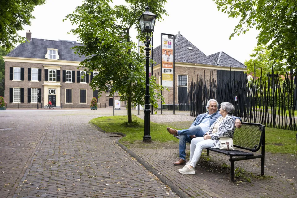 Twee bezoekers zitten op een bankje voor de historische gebouwen van het Drents Museum in Assen