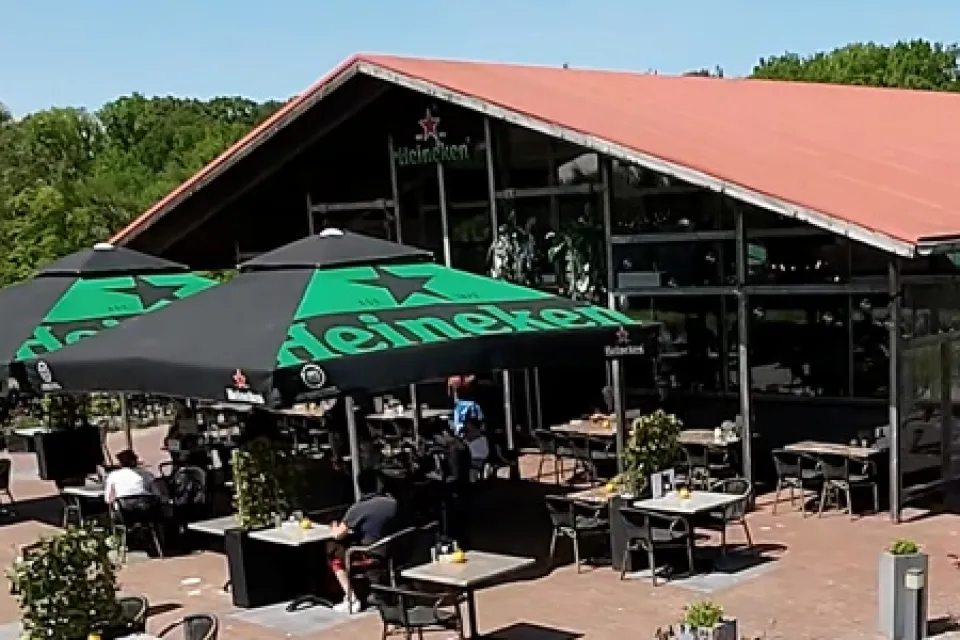 Buitenkant van de brasserie van Buitenplaats de Hildenberg met terras, groene parasols en rieten dak