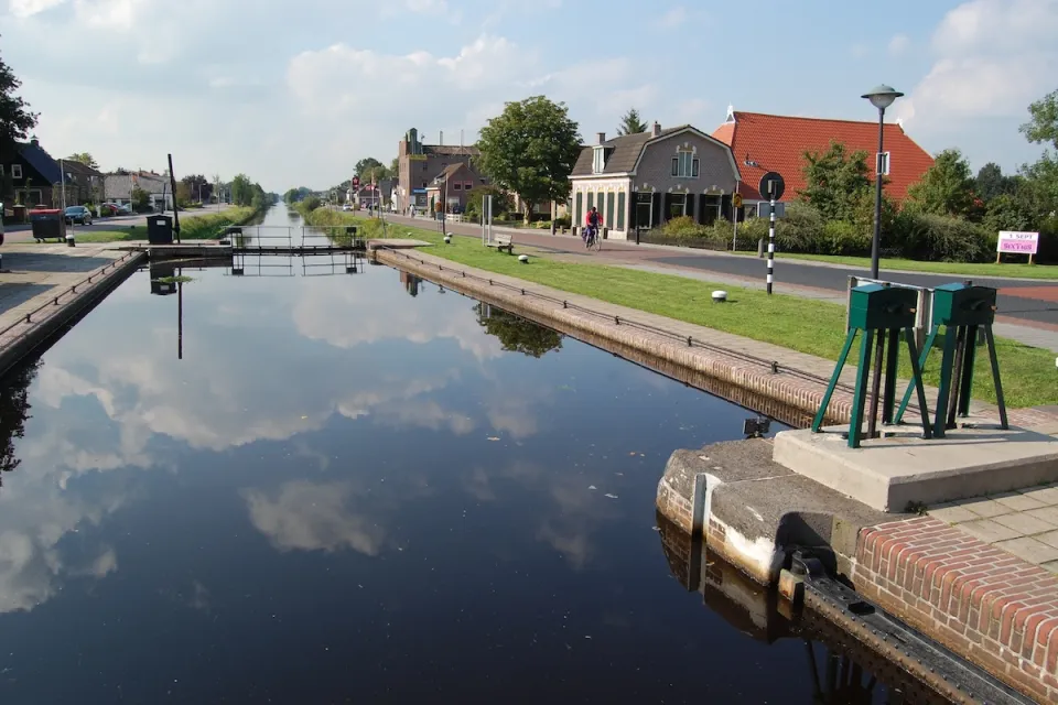 Spiegelend water van de Compagnonsvaart met woningen en een brug in Appelscha