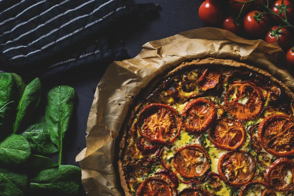 Verse pizza met tomaten en kruiden op een houten plank uit de pizzeria in Appelscha