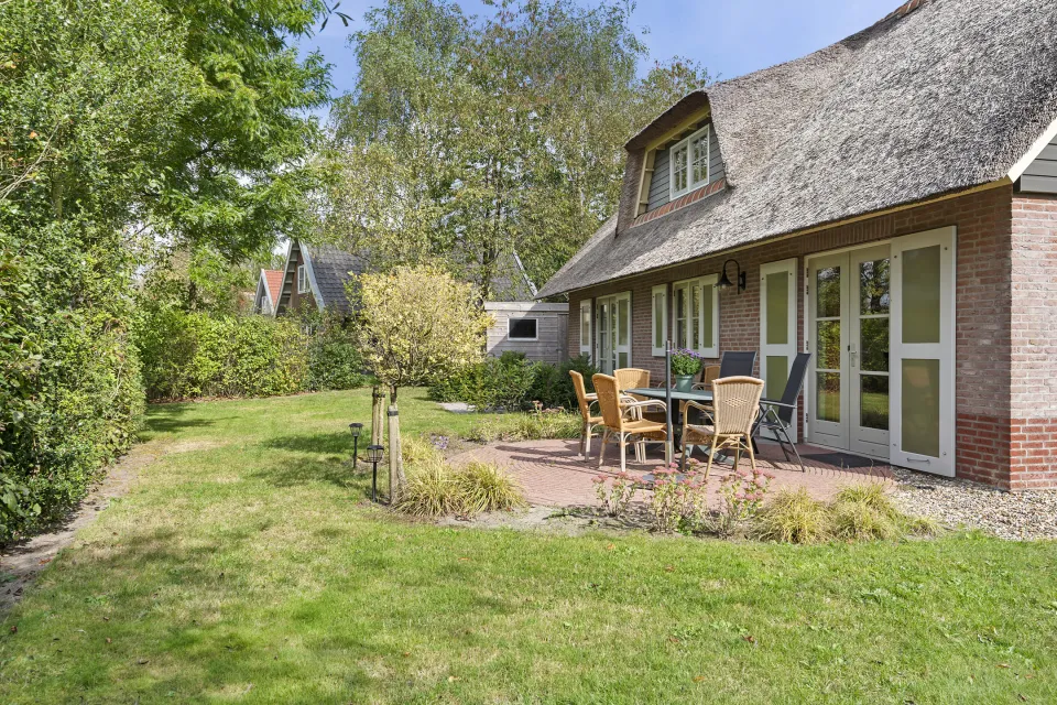 Terras met tuinstoelen en grasveld aan de achterzijde van vakantiewoning Dagpauwoog aan Gruun 28 op Buitenplaats de Hildenberg