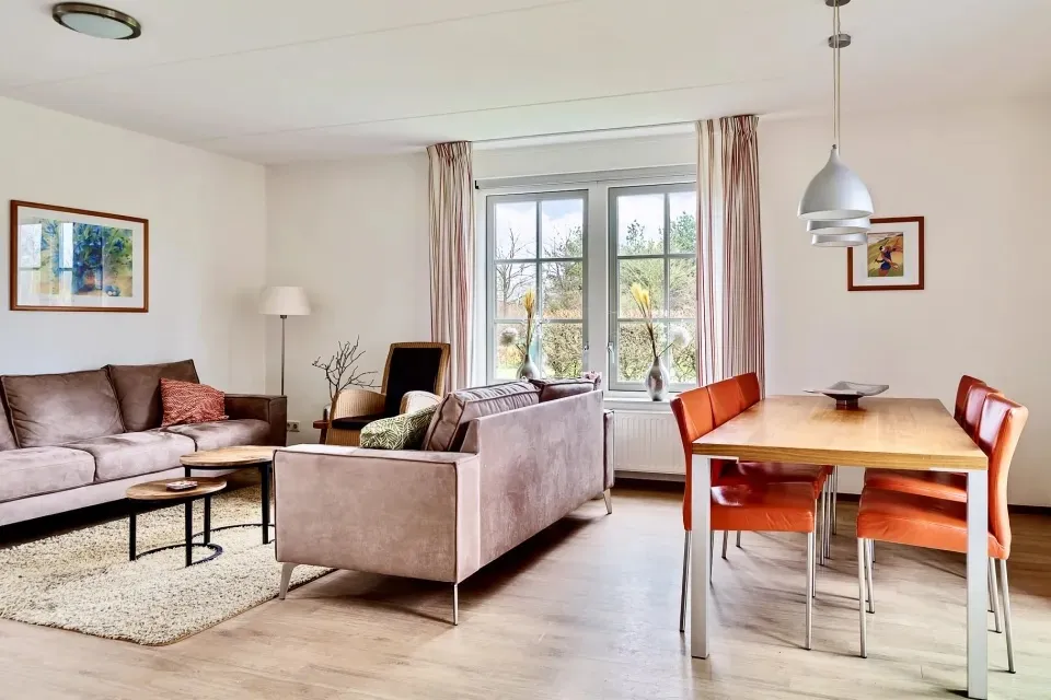 Woonkamer met beige bank, eettafel met rode stoelen en tuindeuren in vakantiewoning Morgenrood aan Ofslag 4