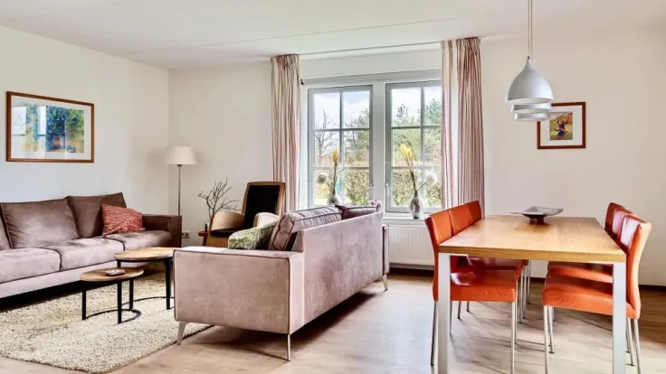 Woonkamer met beige bank, eettafel met rode stoelen en tuindeuren in vakantiewoning Morgenrood aan Ofslag 4